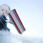 Person scraping ice and snow off of a windshield