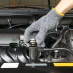 Gloved hand opening a radiator valve on a car engine