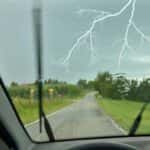 Flash of forked lightning in front of a car during a daytime thunderstorm