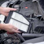 Man's hands holding an engine air filter above an engine compartment