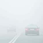Two cars driving in fog on a two-lane road