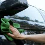 Man's hand using a green cloth to clean a car with waterless wash