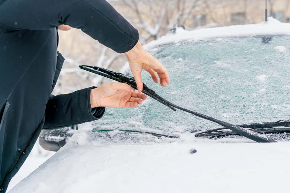 Man lifting wiper blades on an icy and snowy windshield