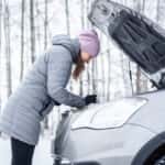 Woman looking under the hood of a vehicle in winter