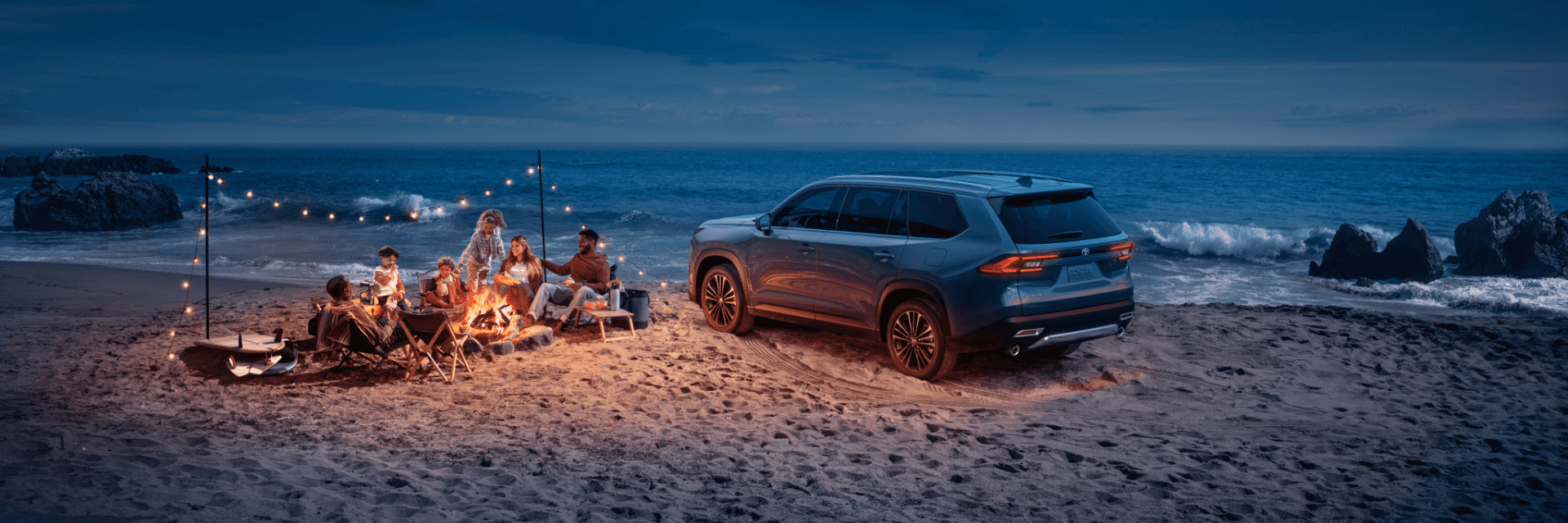 Family having a campfire on the beach next to a Grand Highlander