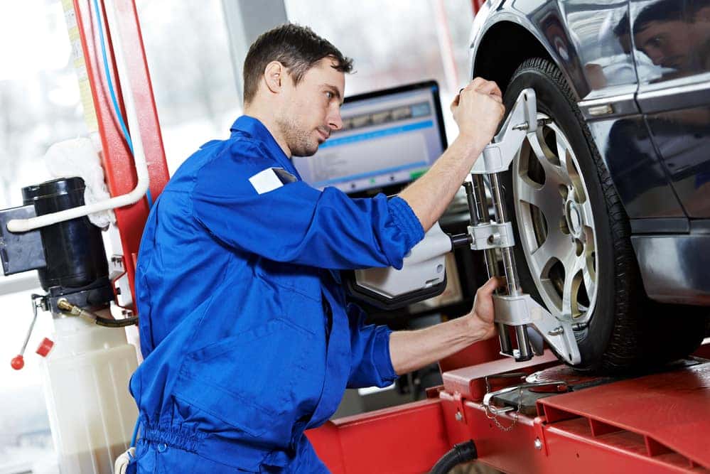 car mechanic installing sensor during suspension adjustment and automobile wheel alignment work at repair service station