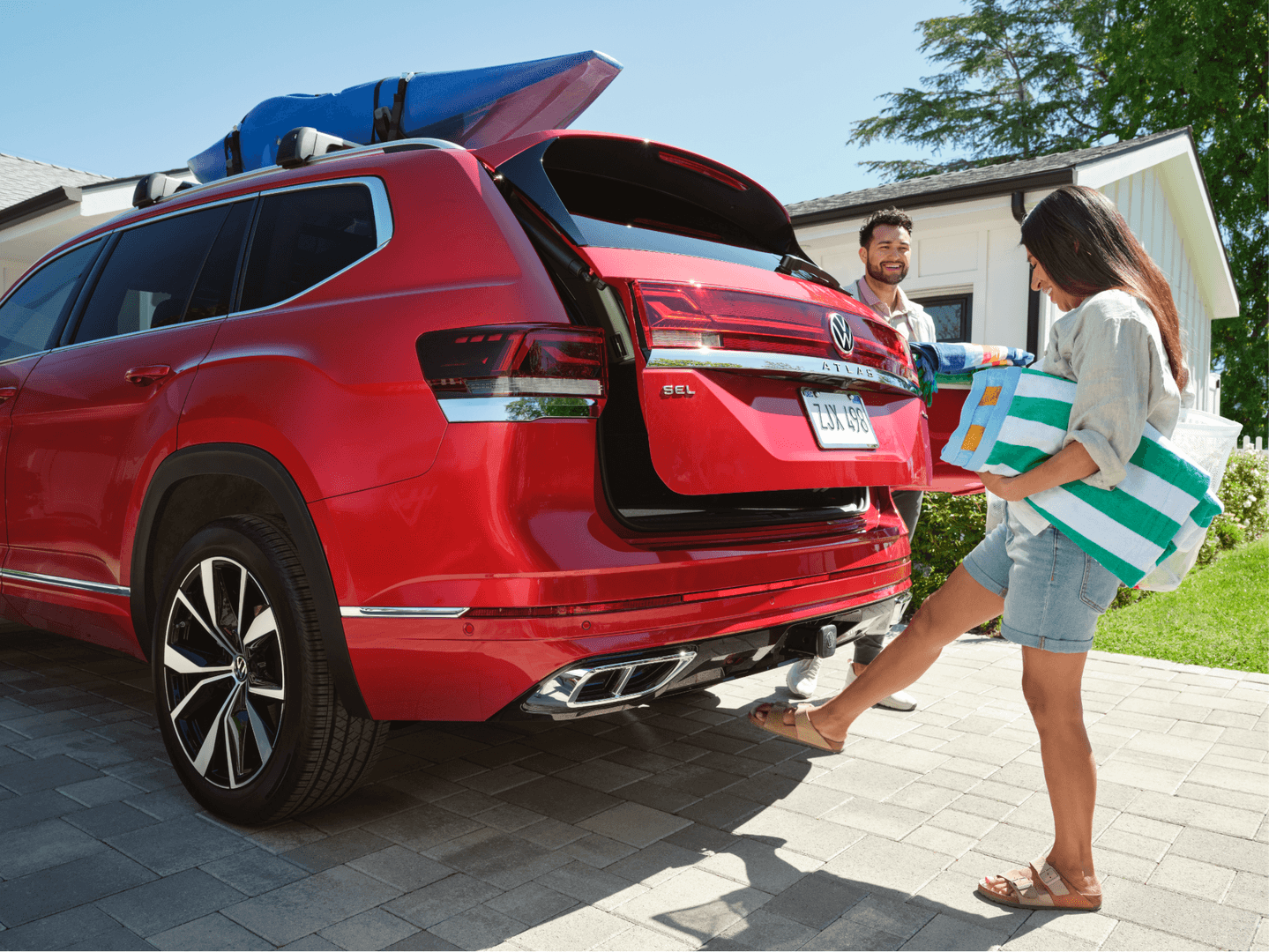 Woman activates hands-free liftgate on red Volkswagen Atlas SUV while carrying beach towels