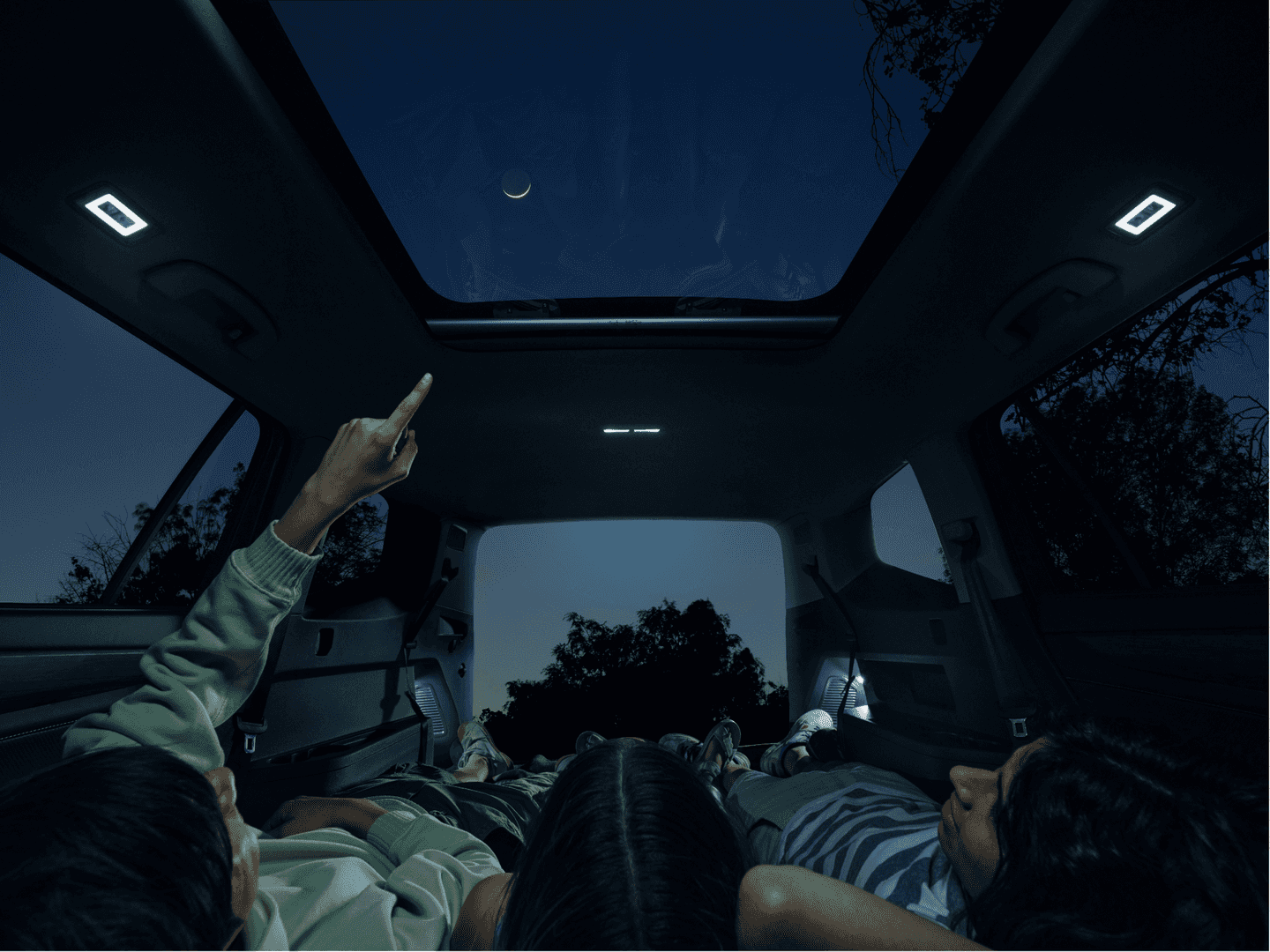 Children laying in the back of a Volkswagen Atlas at night, stargazing through the panoramic sunroof