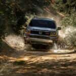 2027 honda passport trailsport edition offroading through a muddy dirt road with water crashing up the sides of the vehicle