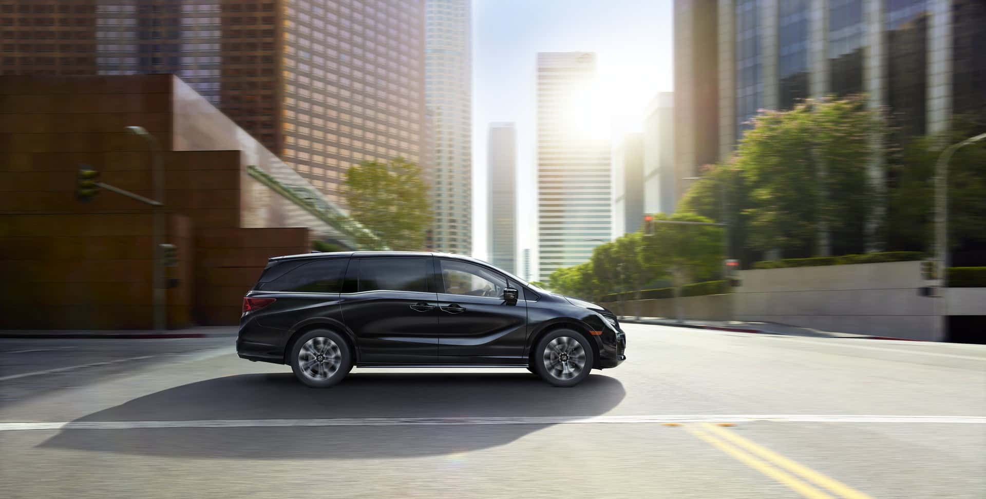 Side view of a black Honda Odyssey minivan driving down a city street