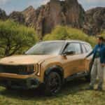 2027 seltos on a patch of grass with a mountain and tree background. A girl is reaching towards the door handle to open the vehicle