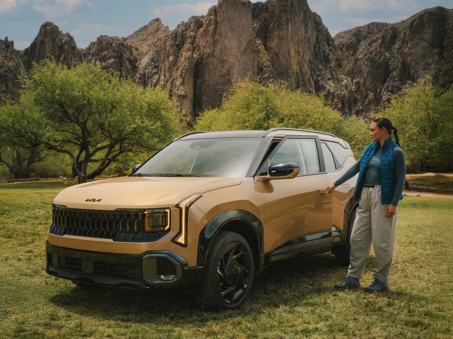 2027 seltos on a patch of grass with a mountain and tree background. A girl is reaching towards the door handle to open the vehicle