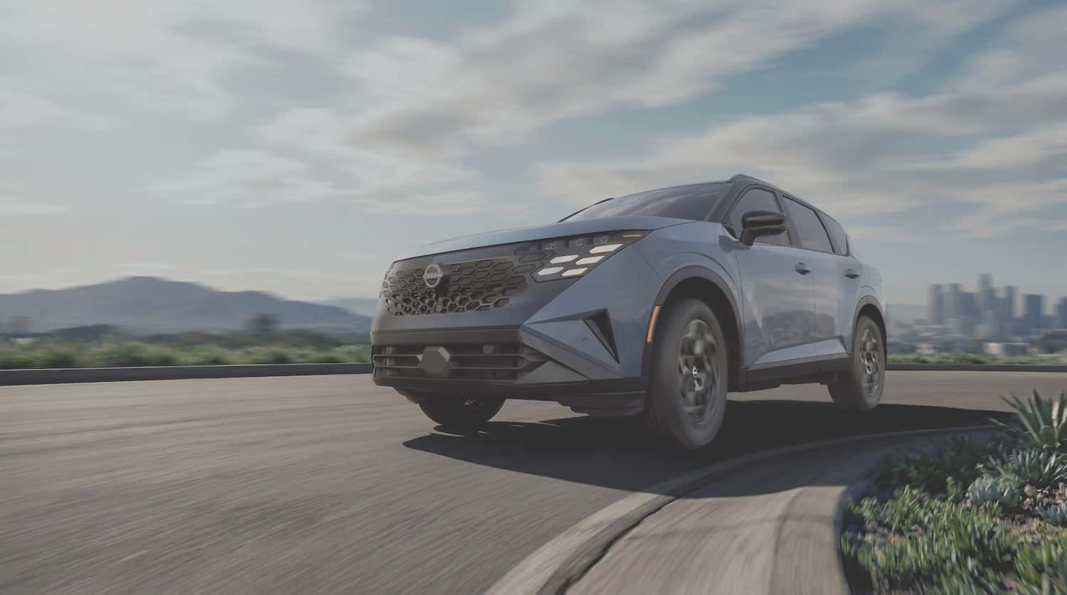 2027 Nissan Rogue Hybrid in blue-gray driving on a curved road with mountains and a city skyline behind it