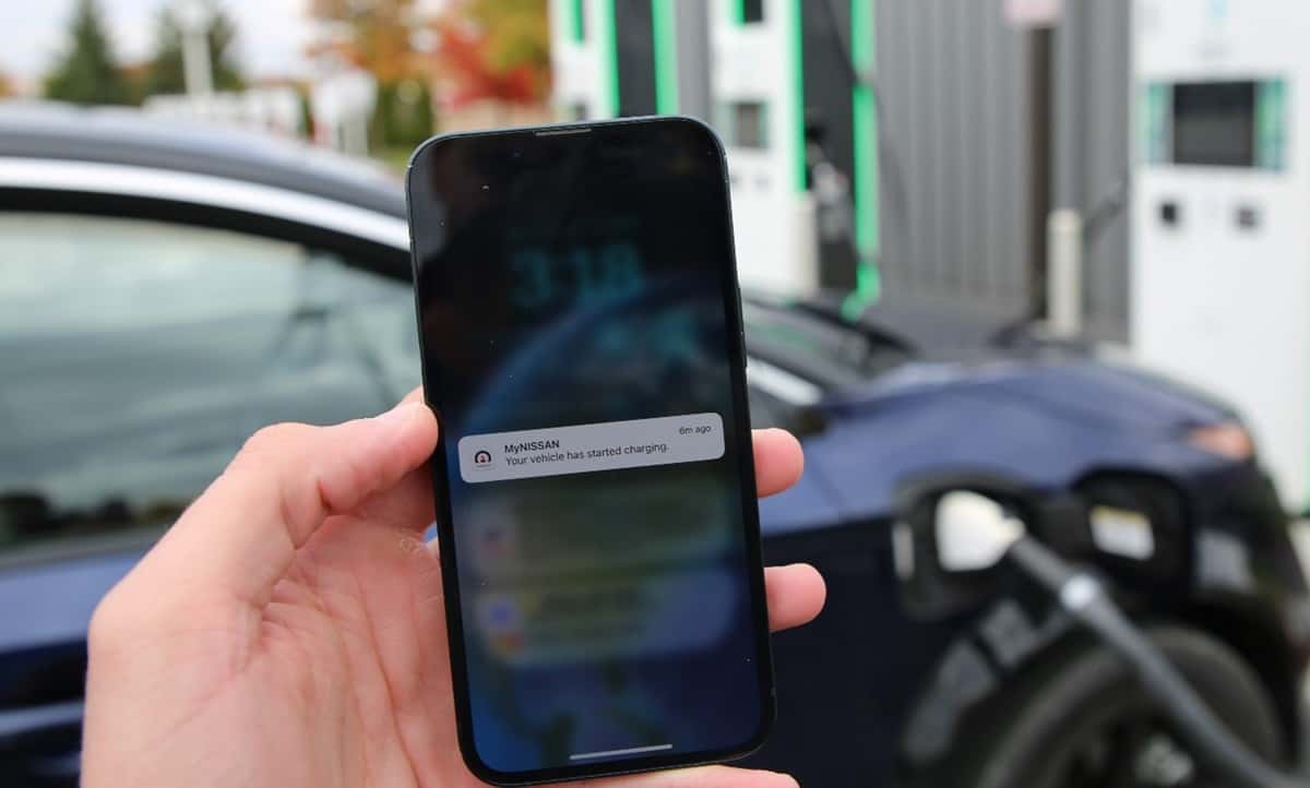 Driver using the MyNISSAN app on a smartphone next to a parked Nissan