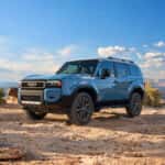 The 2027 Toyota Land Cruiser in Heritage Blue is parked at the top of a barren mountain with a beautiful blue sky with minimal clouds
