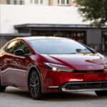 2027 toyota prius in supersonic red driving through a downtown area