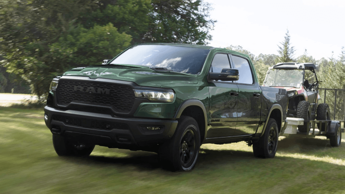 A green RAM 1500 hauling a golf cart over a grassy field