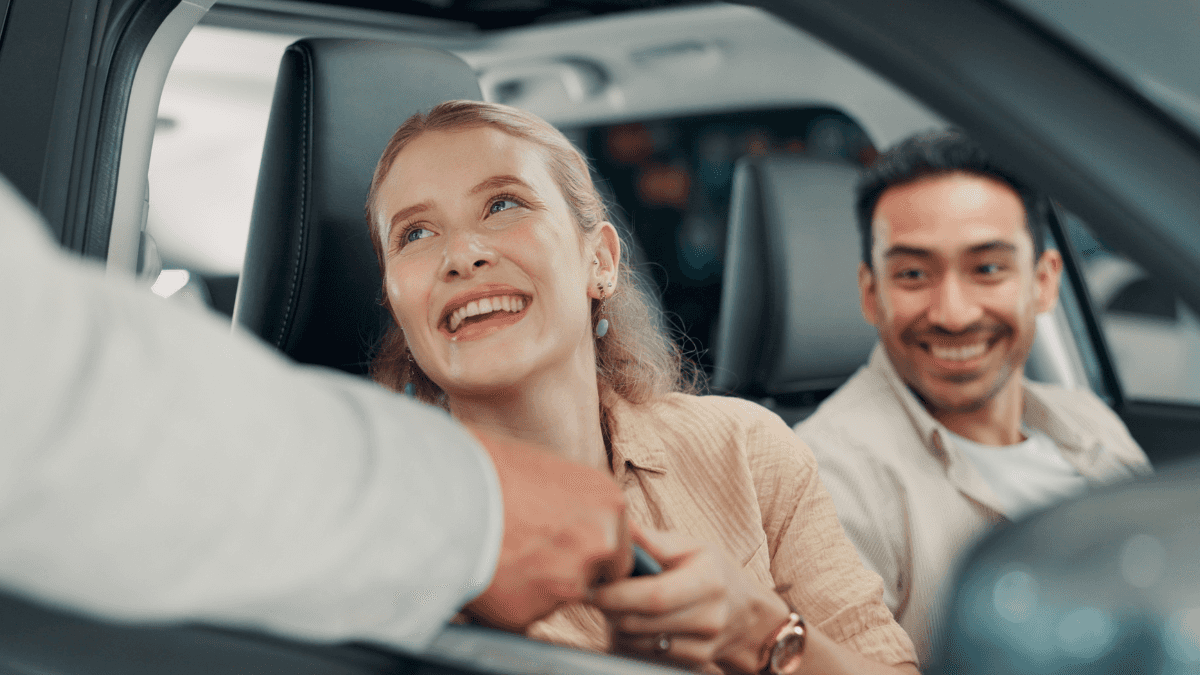 A couple getting the keys to their new car while inside it through the window
