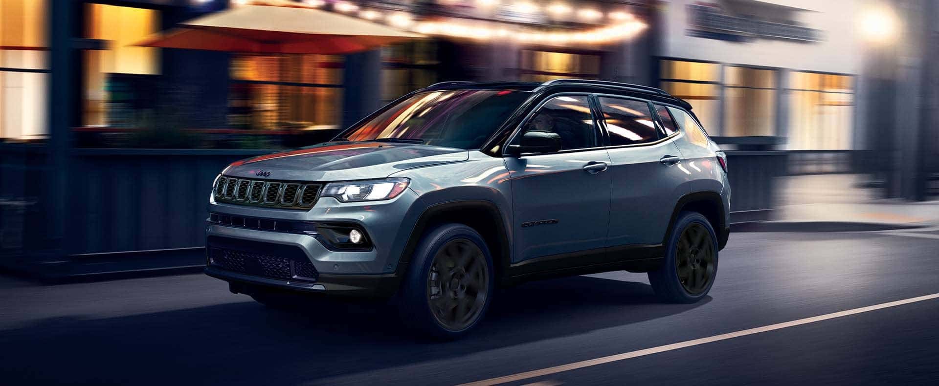 A light blue Jeep Compass driving through a city at night