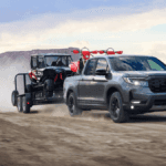 A gray Honda Ridgeline towing a trailer and cart over a dirt road through a ranch