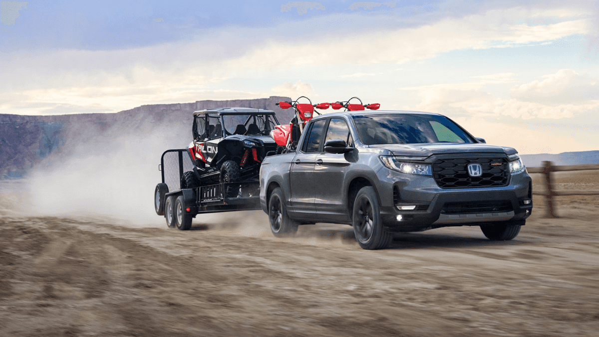 A gray Honda Ridgeline towing a trailer and cart over a dirt road through a ranch