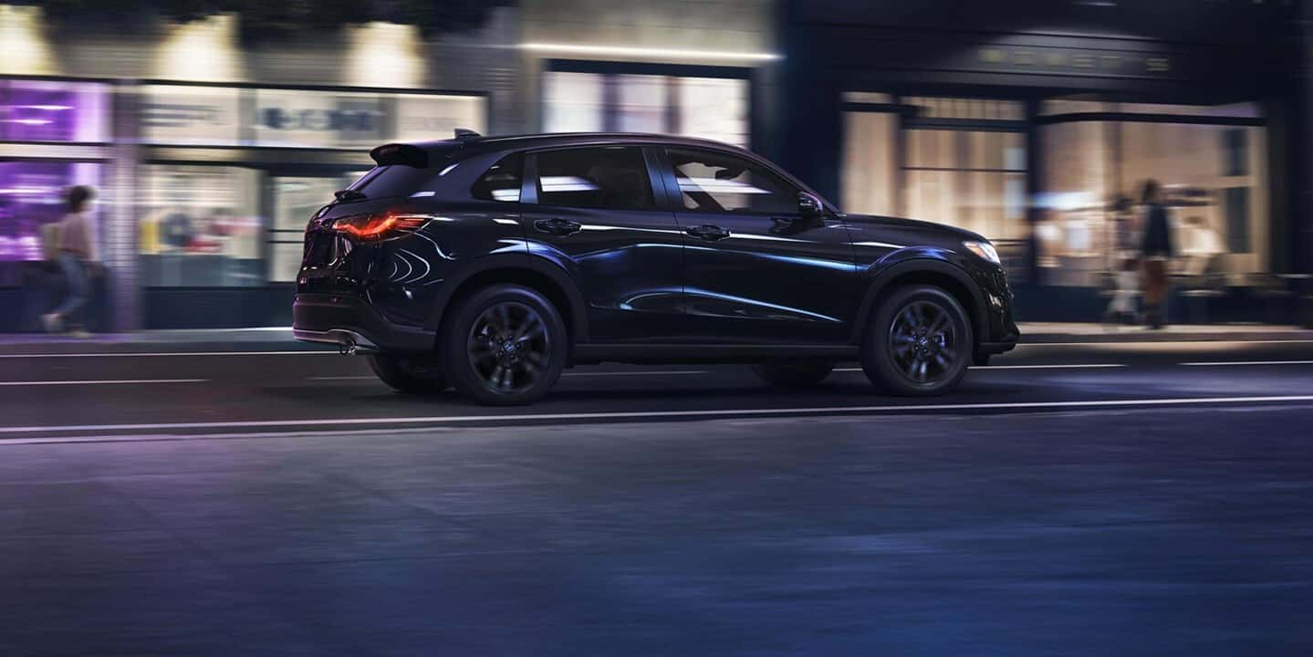 A black Honda HR-V in profile driving down the road at night in a city