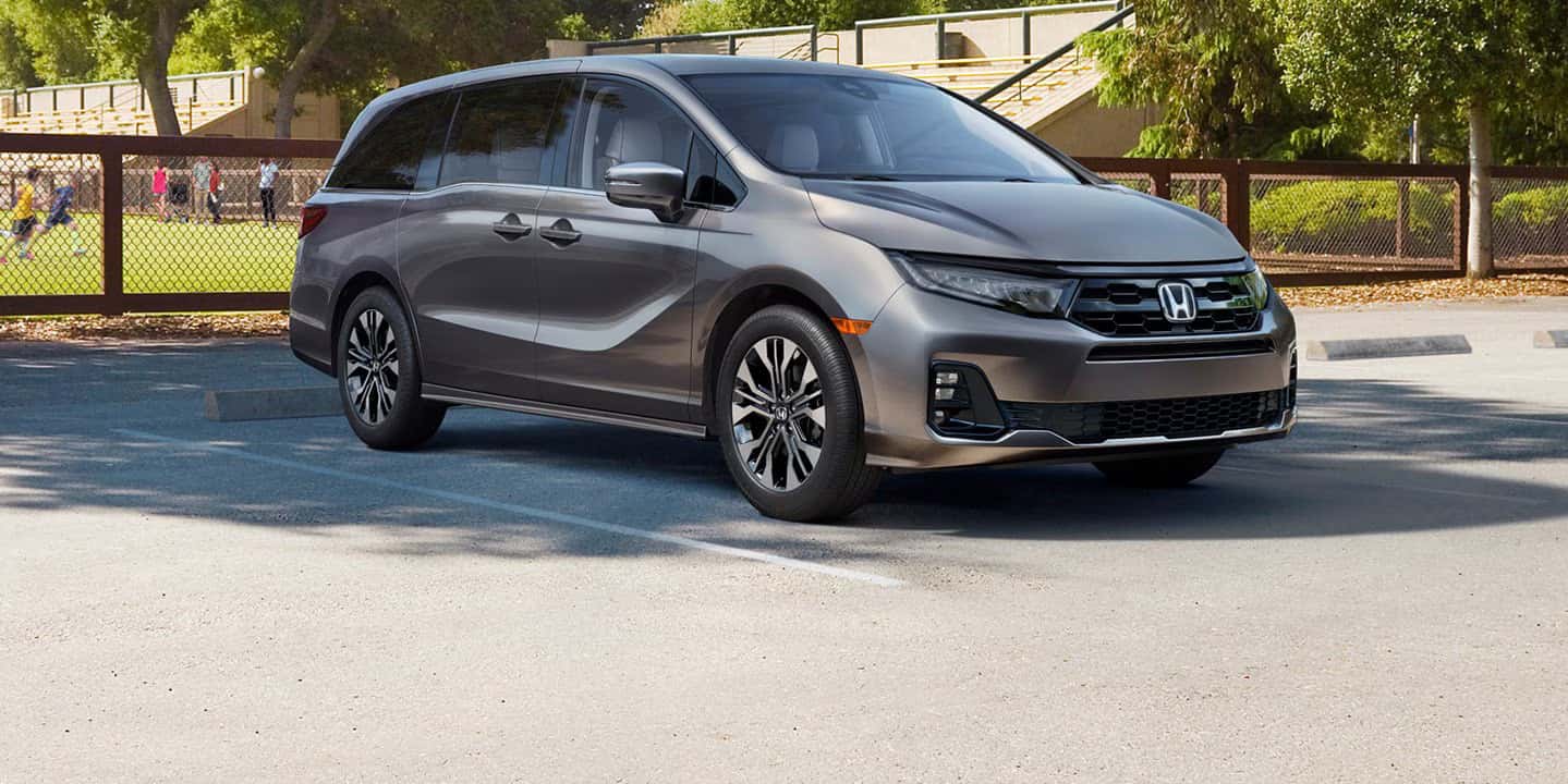 A gray Honda Odyssey parked by a soccer field