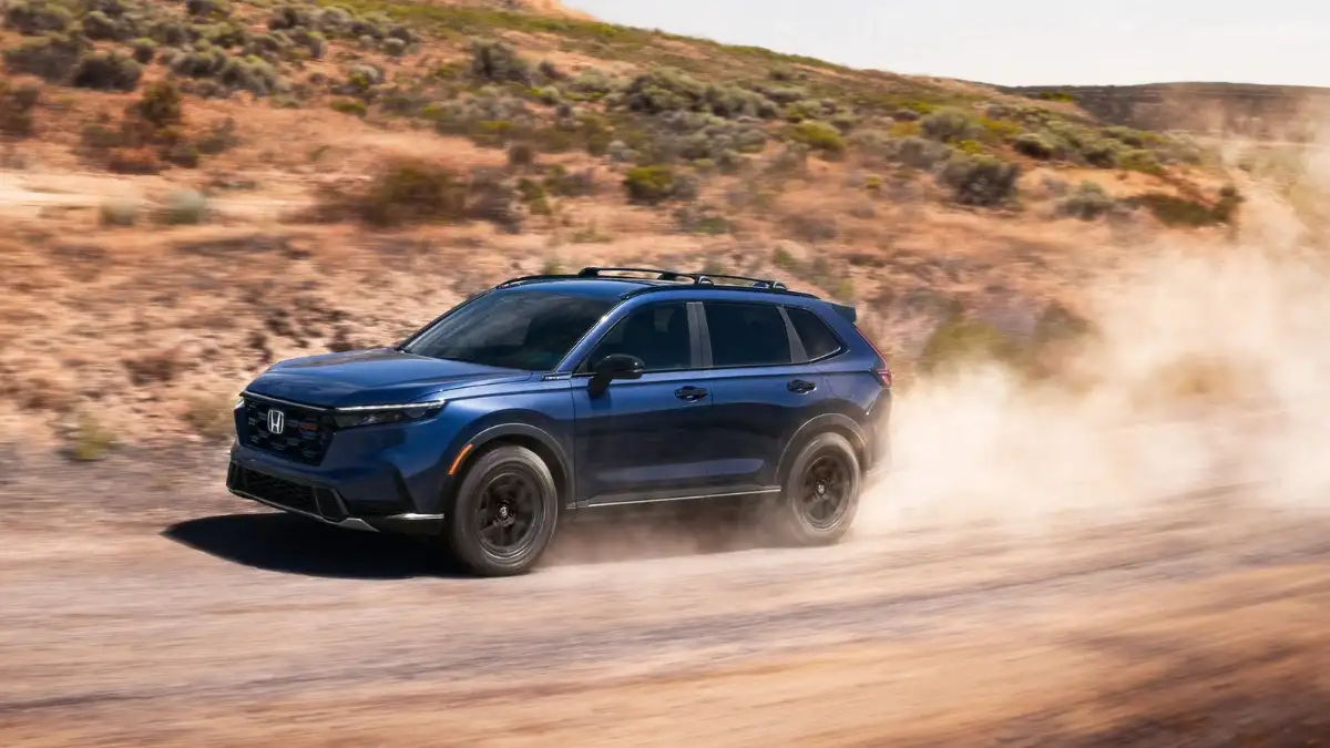 A blue Honda CR-V driving on a dirt road and kicking up dust in a desert