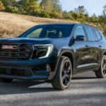 Black 2025 GMC Acadia Elevation driving on a country road