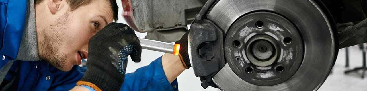 View of a service tech inspecting a brake pad on a vehicle