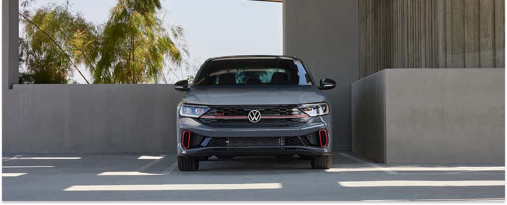 Front view of a grey 2026 Volkswagen Jetta GLI parked in a modern concrete structure.