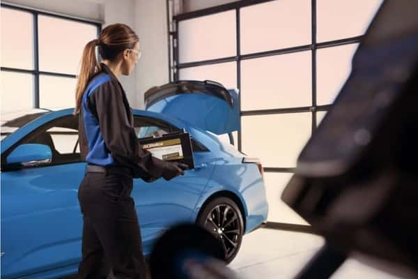 Cadillac-certified technician carrying a genuine ACDelco battery during vehicle battery inspection and replacement service.