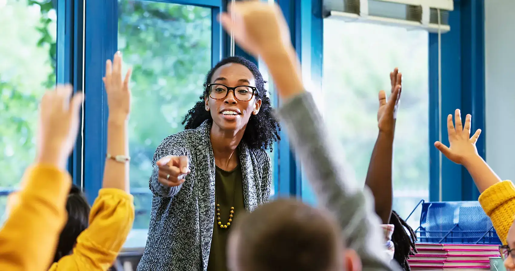 Teacher in a classroom with students raising their hands