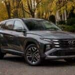 2026 Hyundai Tucson Hybrid in Ecotronic Gray parked on tree-lined autumn road — Webb Hyundai Highland serving Highland, Munster, and Hammond, IN