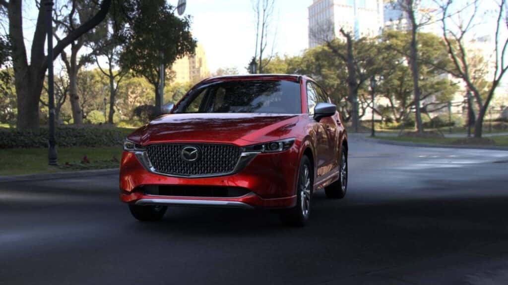 2025 Mazda CX-50 in red driving on city street during the holidays