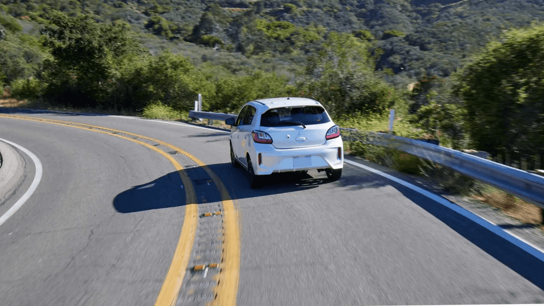 2024 Mitsubishi Mirage rear exterior driving on winding mountain road showing compact hatchback design and LED taillights