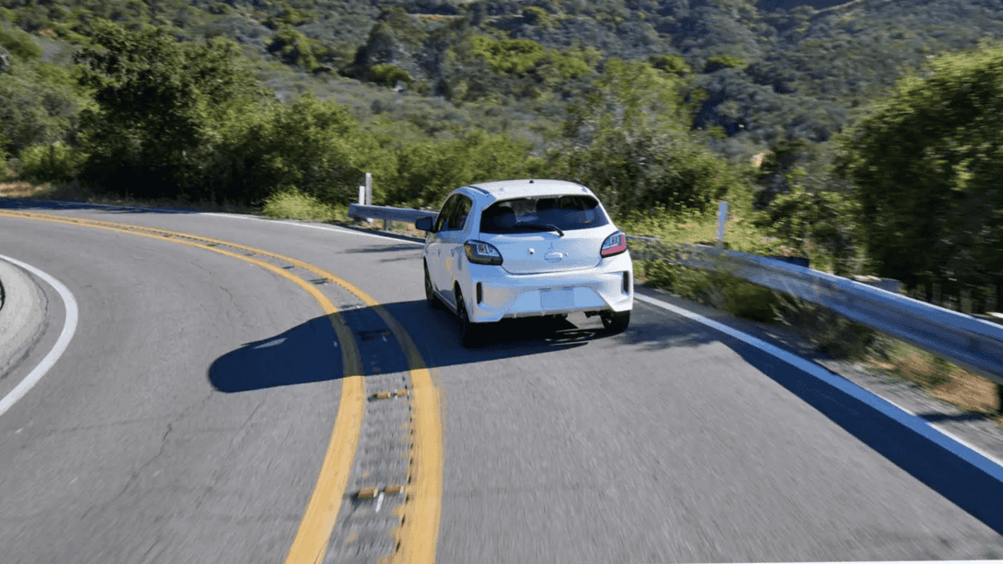 2024 Mitsubishi Mirage rear exterior driving on winding road highlighting hatchback design and taillights