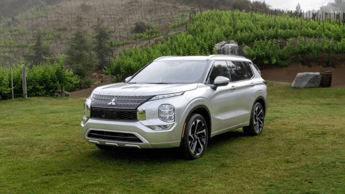 2024 Mitsubishi Outlander front three quarter exterior in silver on grassy landscape highlighting SUV stance, alloy wheels, and modern lighting