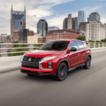 2025 Mitsubishi Outlander Sport front three quarter exterior in red driving across bridge highlighting compact SUV stance and LED lighting