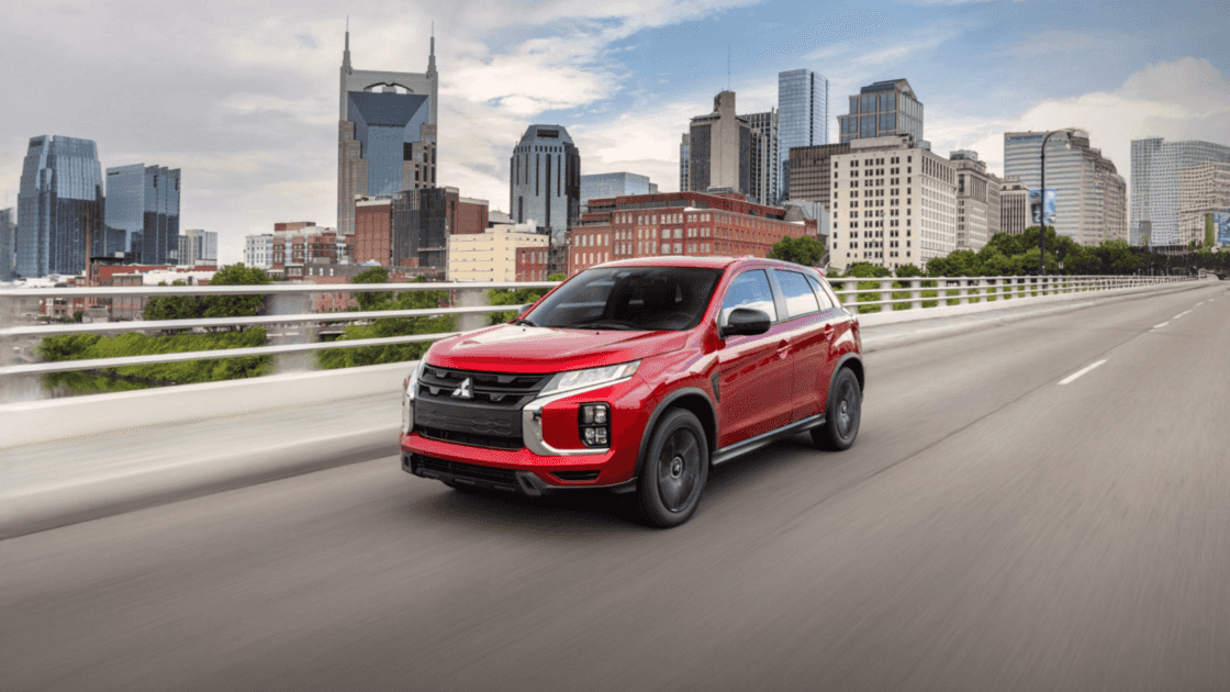 2025 Mitsubishi Outlander Sport front three quarter exterior in red driving across bridge highlighting compact SUV stance and LED lighting