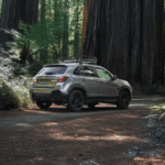 2025 Mitsubishi Outlander Sport rear three-quarter view driving through forest road in silver