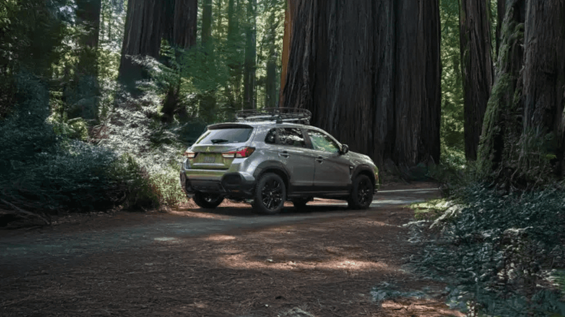 2025 Mitsubishi Outlander Sport rear three-quarter view driving through forest road in silver