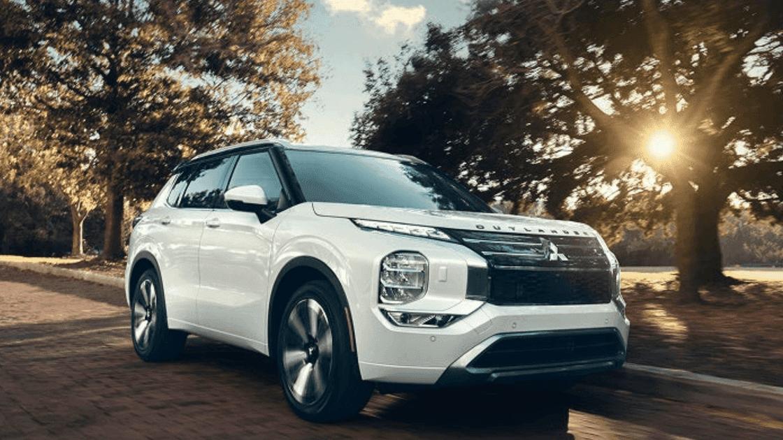 Front exterior view of white 2026 Mitsubishi Outlander SUV on tree-lined road