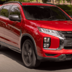2026 Mitsubishi Outlander Sport red SUV driving on road with black grille and roof rails