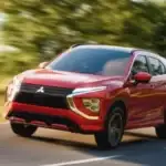 2026 Mitsubishi Eclipse Cross red SUV driving on a curving road with blurred green trees behind