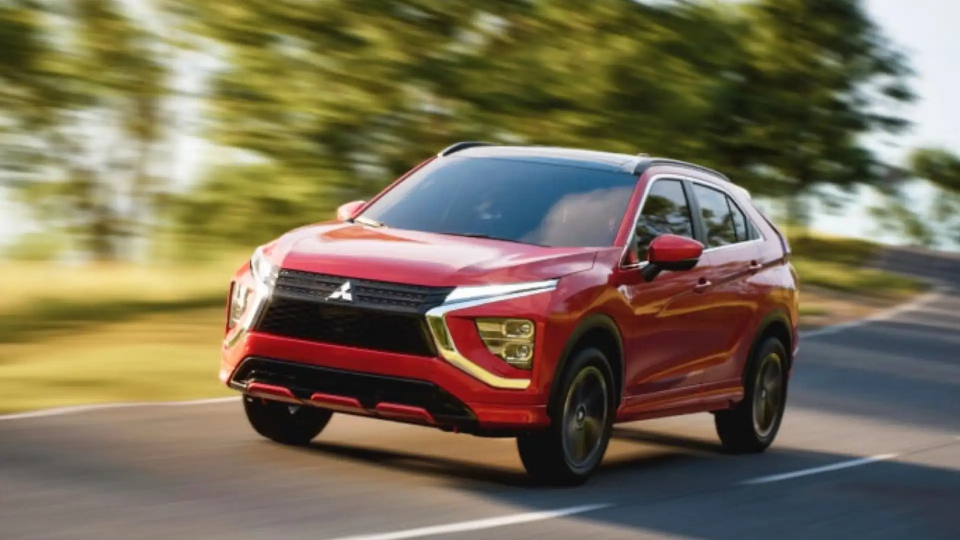 2026 Mitsubishi Eclipse Cross red SUV driving on a curving road with blurred green trees behind