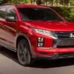 2026 Mitsubishi Outlander Sport red SUV driving on tree-lined road with black wheels and roof rails