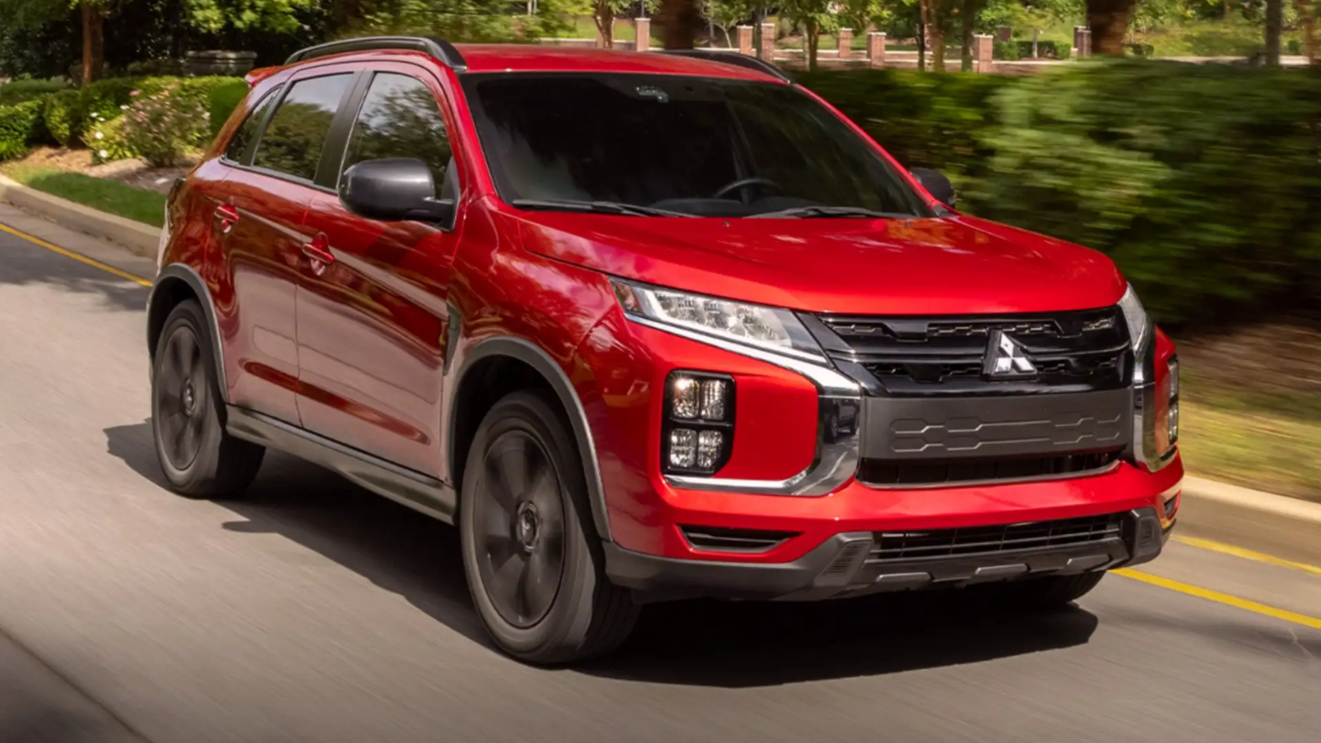 2026 Mitsubishi Outlander Sport red SUV driving on tree-lined road with black wheels and roof rails