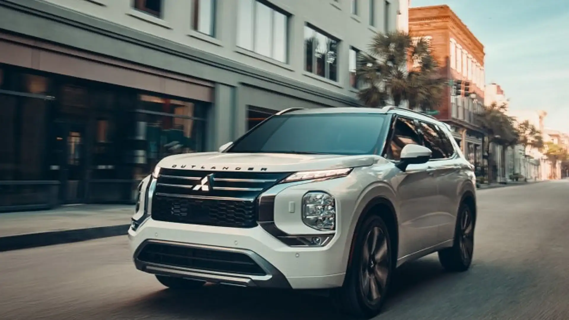 2026 Mitsubishi Outlander white SUV driving through city street with chrome grille and roof rails