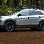 2026 Mitsubishi Outlander Sport silver SUV side profile parked in forest with black wheels and rack